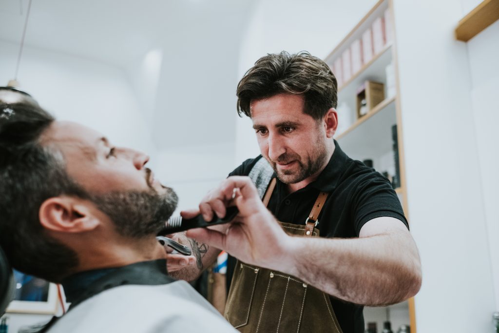 Barber cutting beard to man in salon
