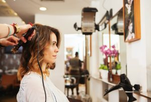 A Complete Guide on Choosing the Best Unisex Salon in Indiranagar Hairdresser using curling tongs on customer's long brown hair in salon